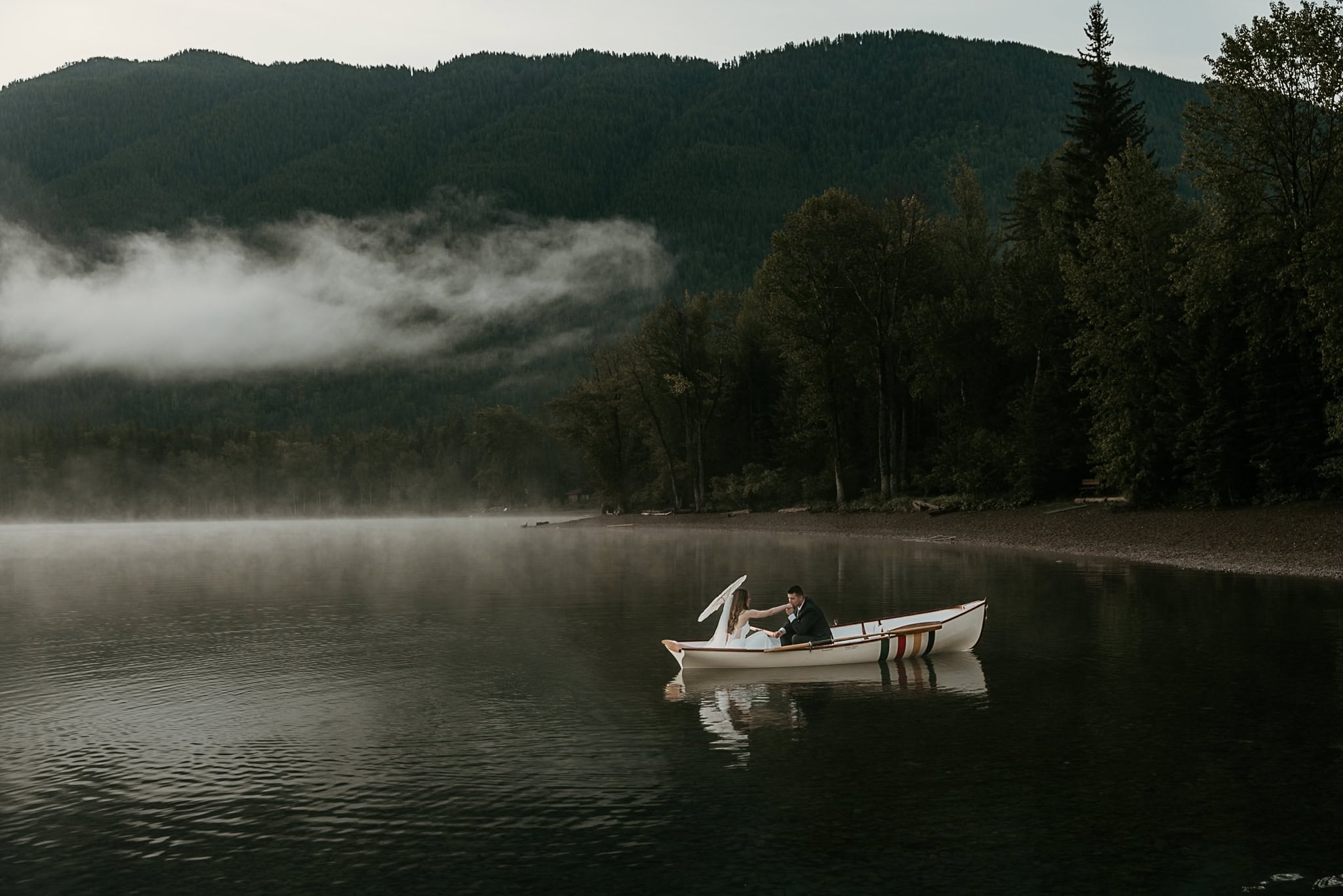 A bride and groom paddle across Apgar Lake during their elopement in Glacier National Park.