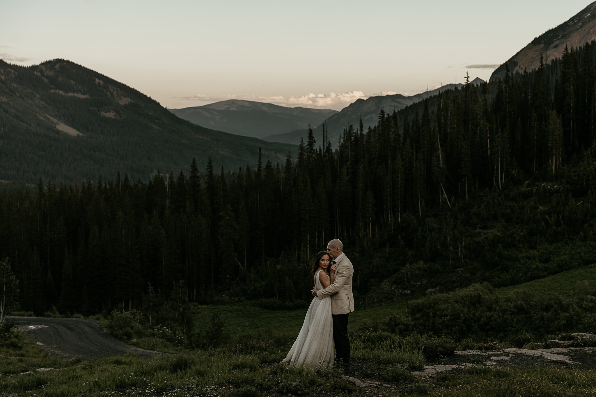 An eloping couple embraces during blue hour in front of the mountains.