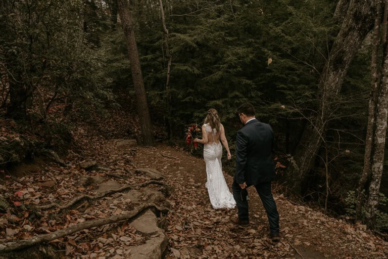 An eloping couple walks down a leaf covered trail.