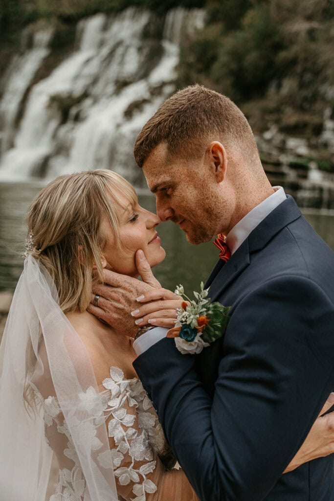 A couple touches their noses together during their outdoor wedding.