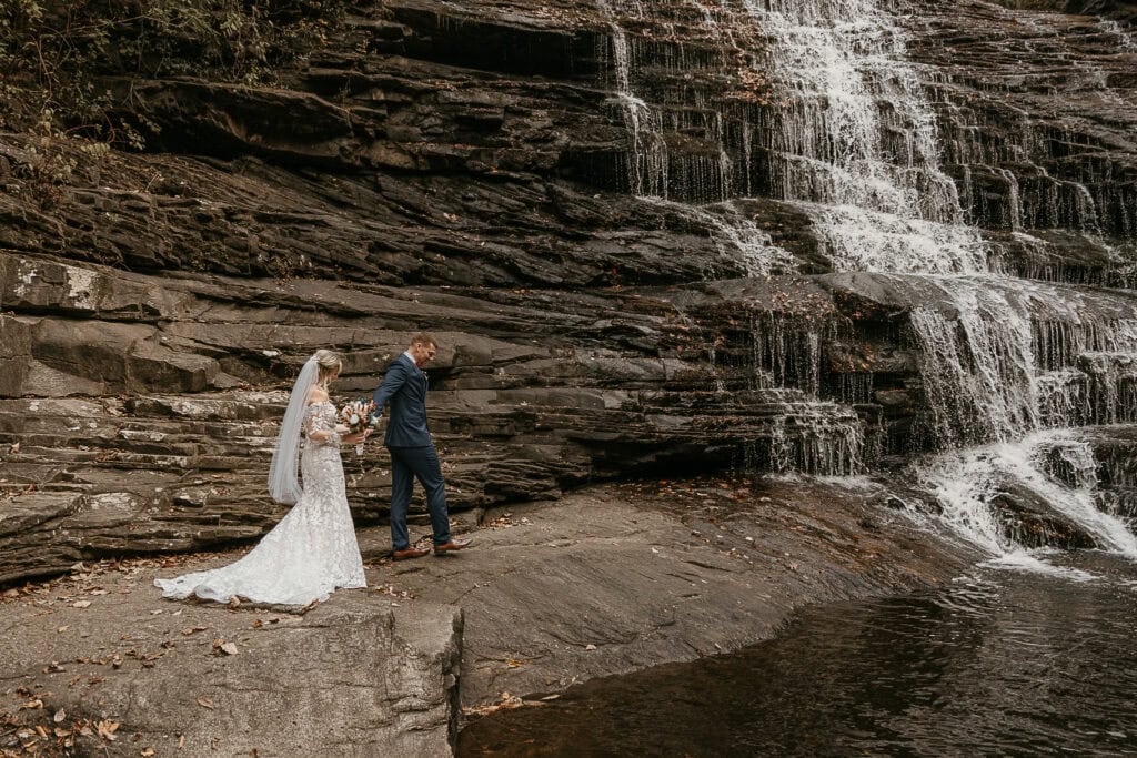 A couple walks hand in hand along the base of a waterfall during their elopement.