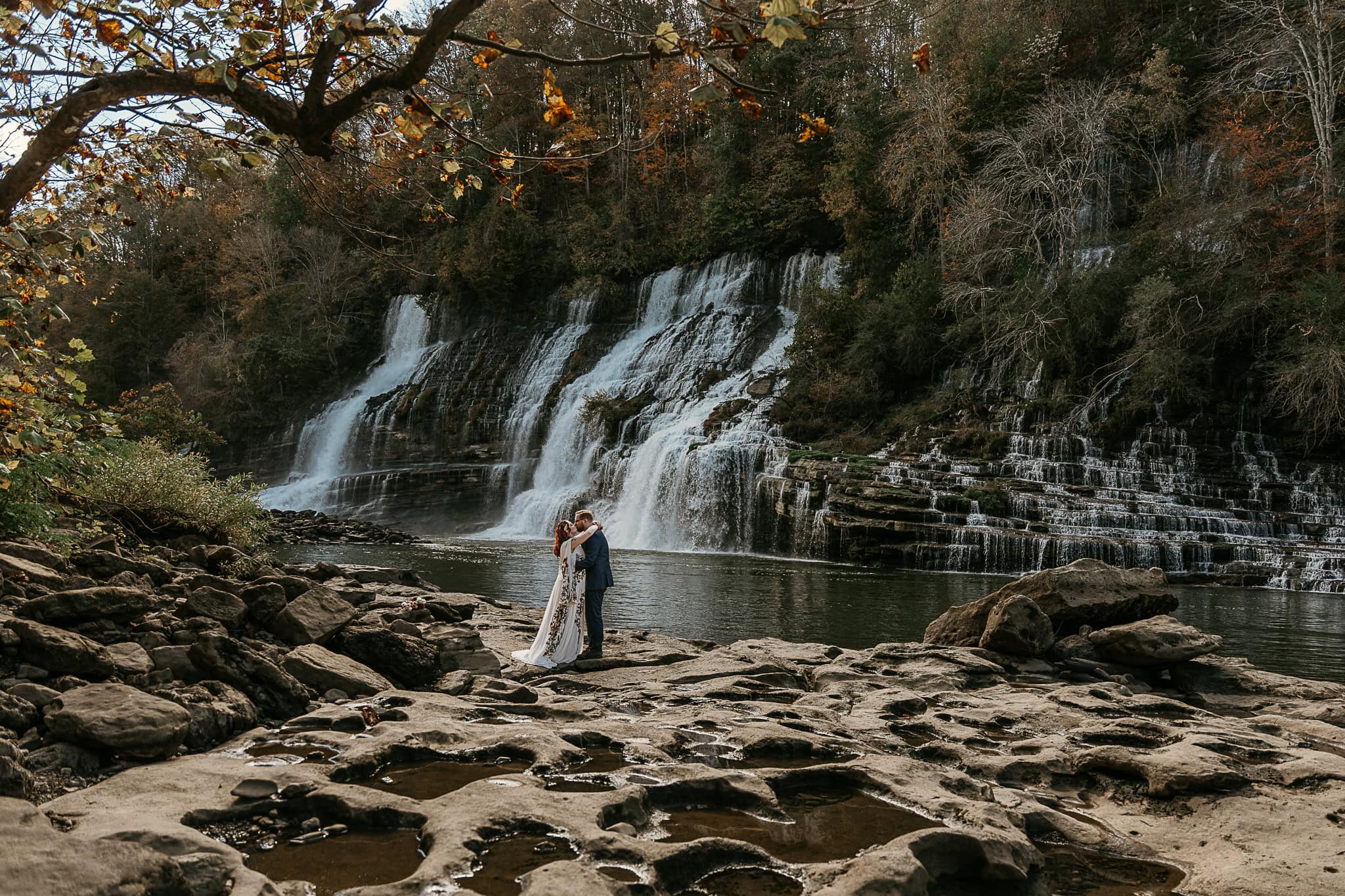 A couple shares a passionate embrace during their elopement. Twin Falls is in the background.
