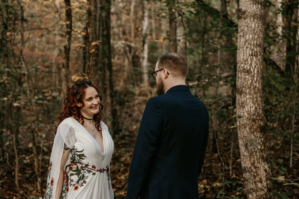 A couple stands facing each other in the forest during their elopement.