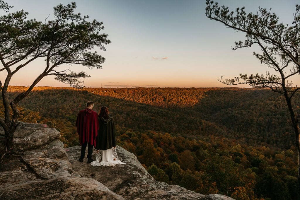 A couple stands on an overlook watching the sunset in autumn,