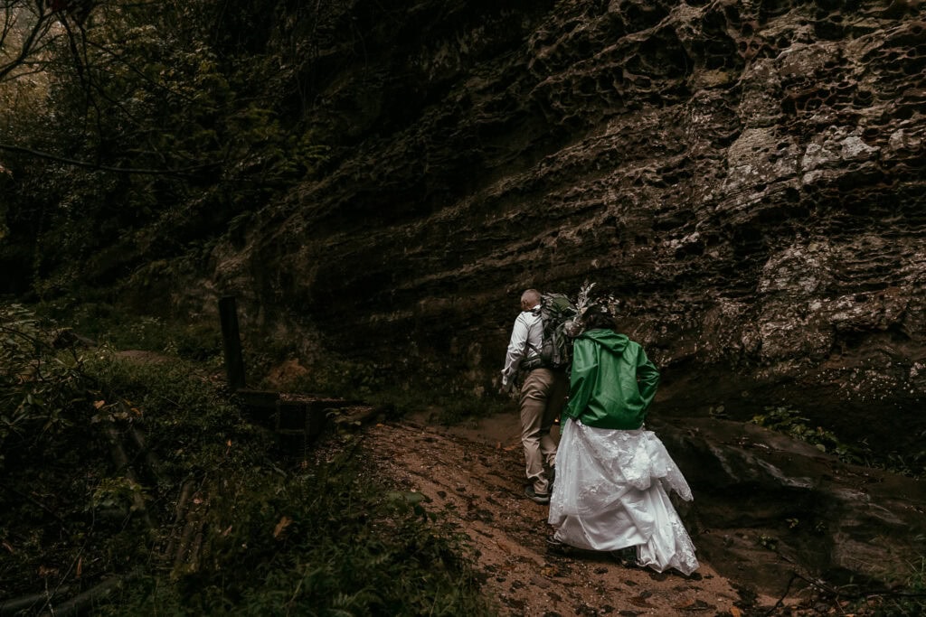 A couple hikes the Natural Bridge trail in wedding attire.