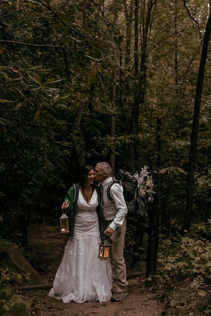 A groom kisses the bride on the cheek as they take a break from hiking during their elopement.