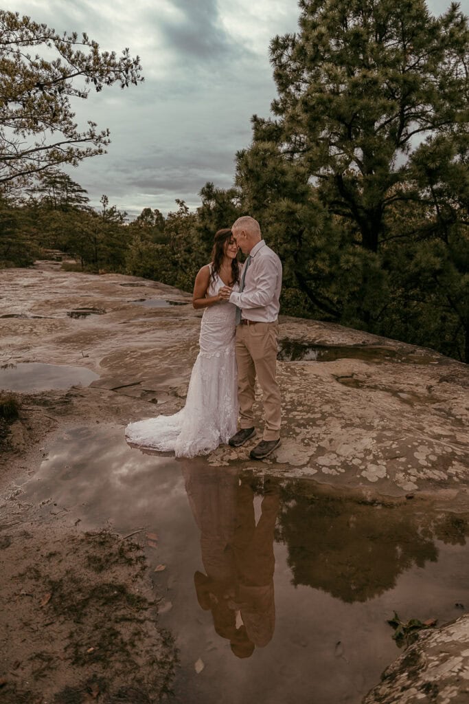 A couple in wedding attire is reflected in a puddle on the rocks.