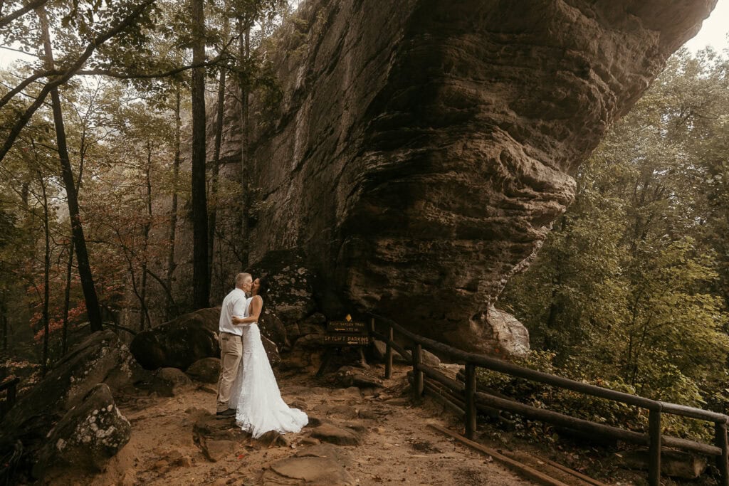 A newly married couple share a kiss under Kentucky's Natural Bridge. Fall colors are in the background.