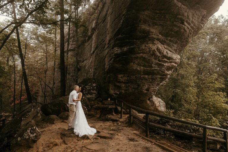 A newly married couple share a kiss under Kentucky's Natural Bridge. Fall colors are in the background.